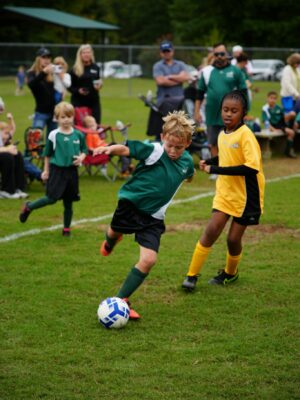 Boys and girls in team soccer jerseys playing soccer on a green field outdoors.